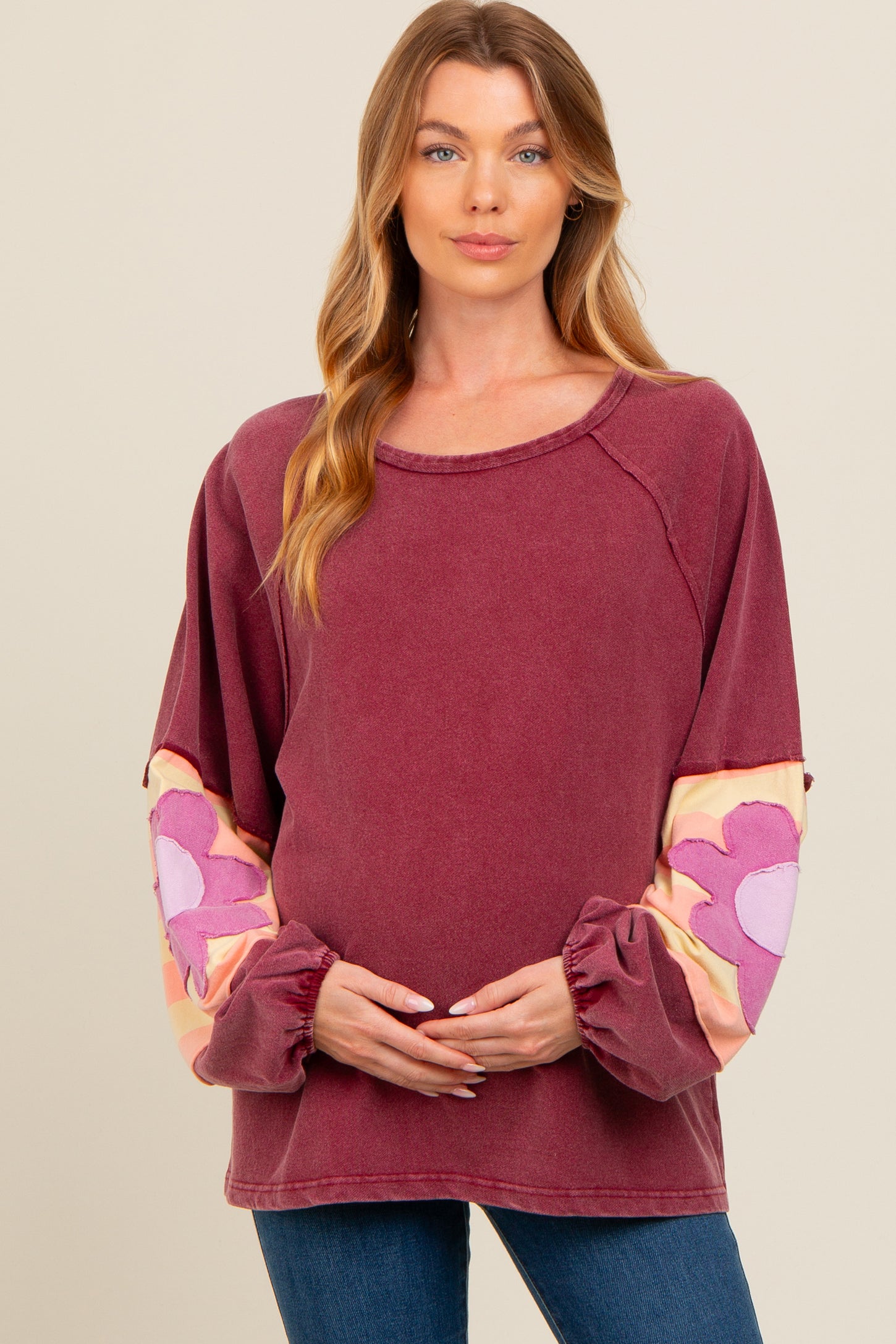 woman wearing a burgundy maternity sweatshirt with floral patterned sleeves and holding her baby bump