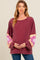 woman wearing a burgundy maternity sweatshirt with floral patterned sleeves and holding her baby bump