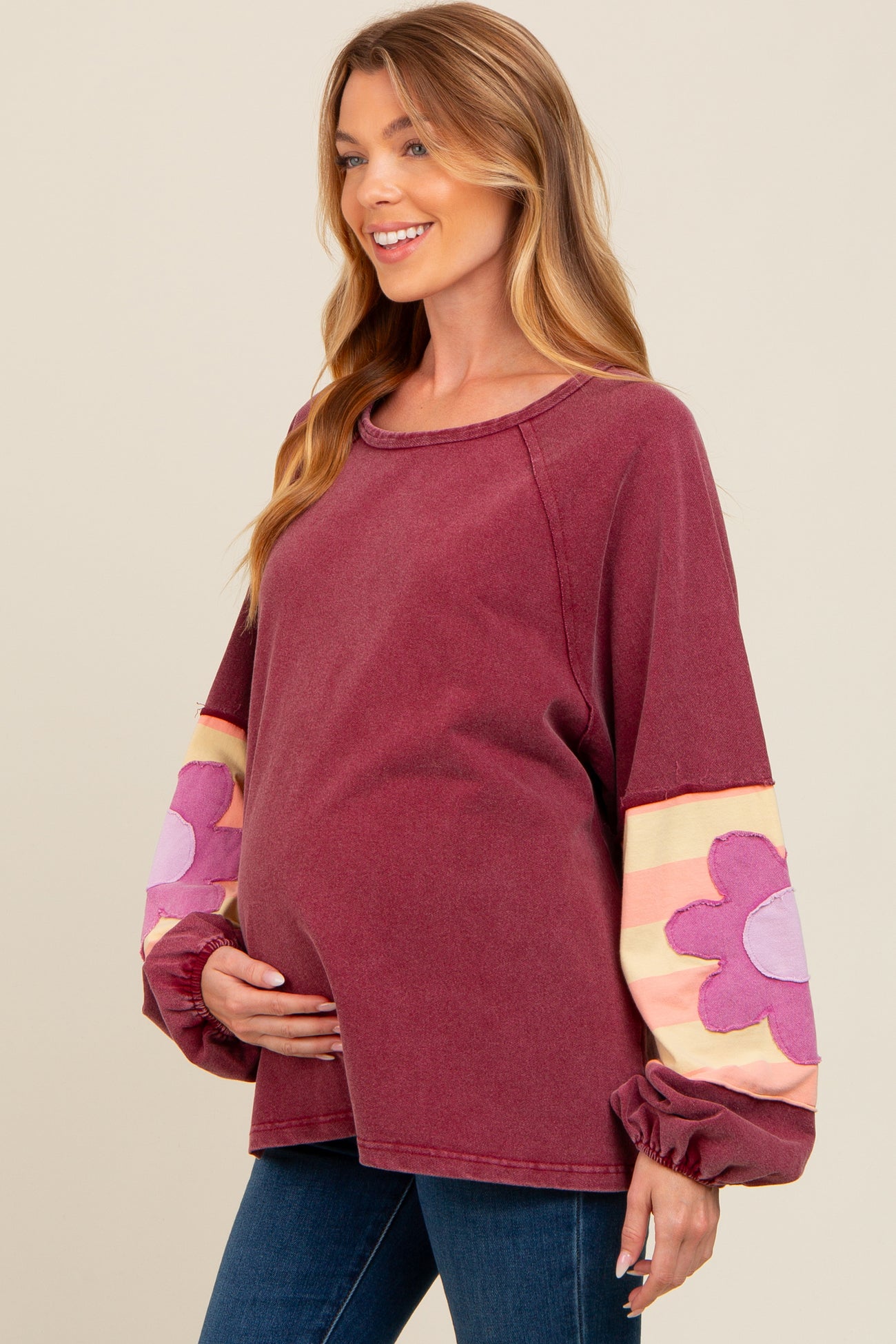 woman wearing a burgundy maternity sweatshirt with floral patterned sleeves and holding her baby bump
