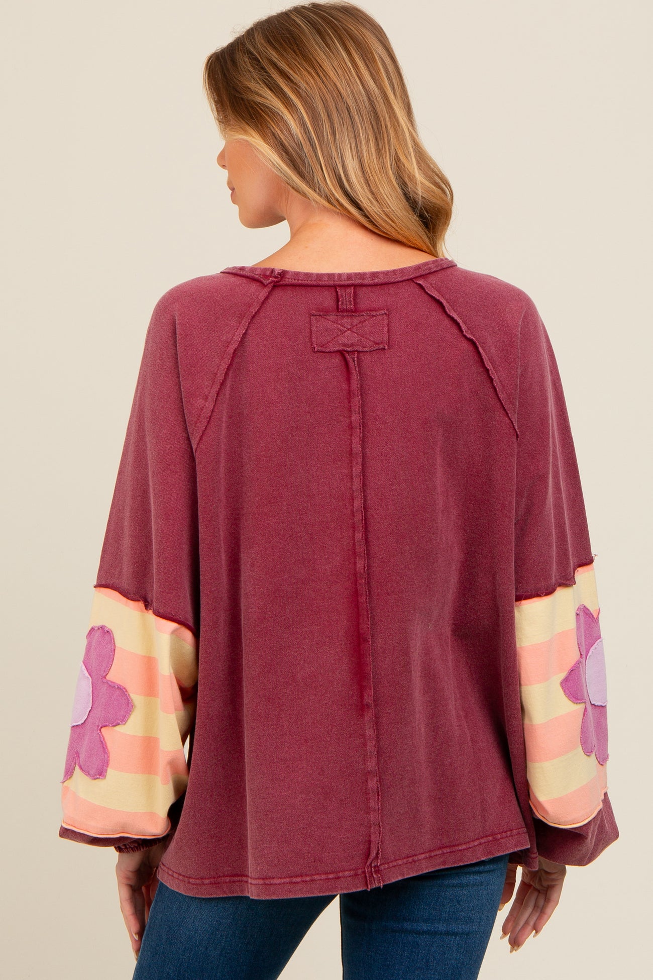 woman wearing a maroon maternity top with floral patterned sleeves and a relaxed fit, showing her back