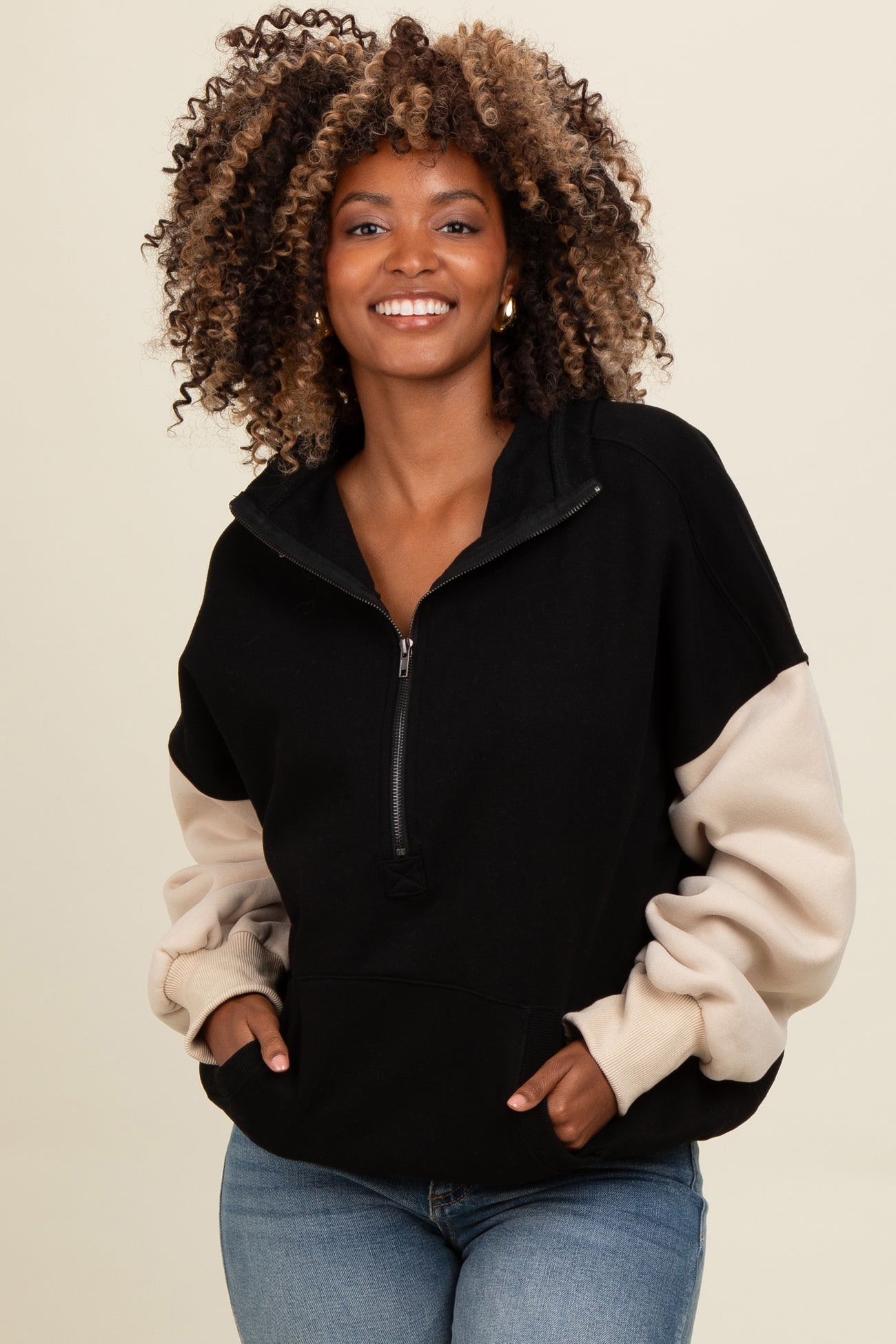 woman wearing a black and beige color block zip-up sweatshirt with a relaxed fit and curly hair