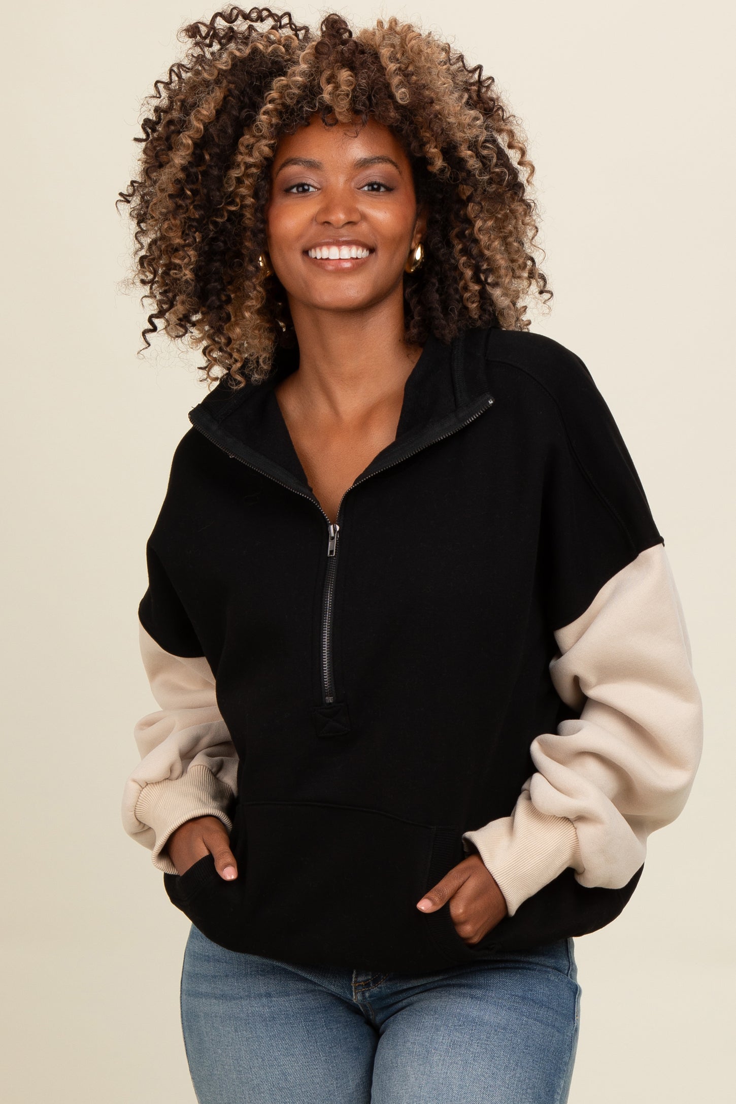 woman wearing a black and beige color block zip-up sweatshirt with a relaxed fit and curly hair