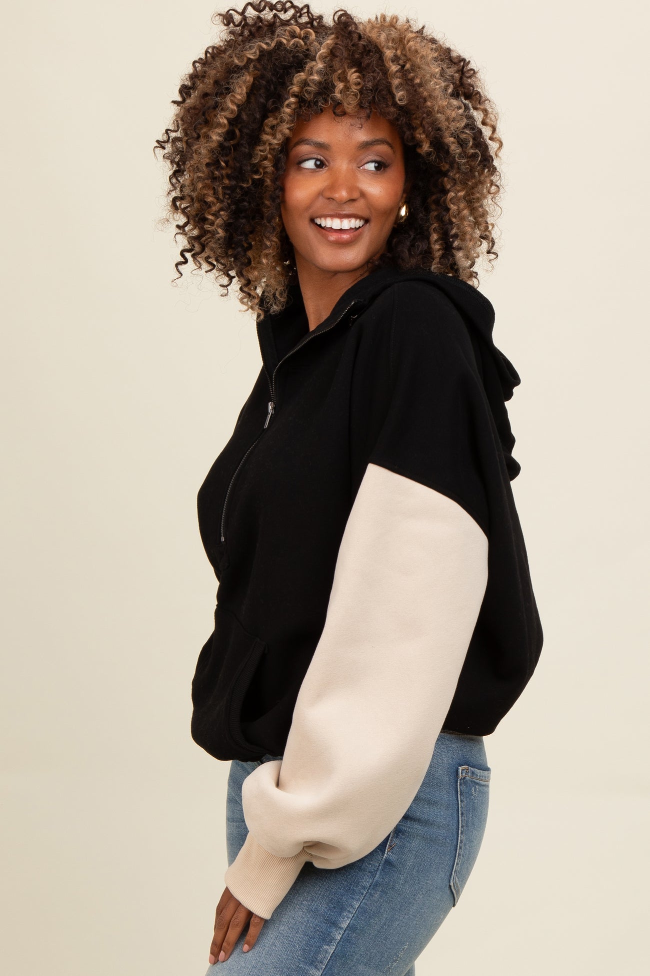 woman wearing a black and beige colorblock hoodie with a cropped fit and large sleeves, smiling to the side