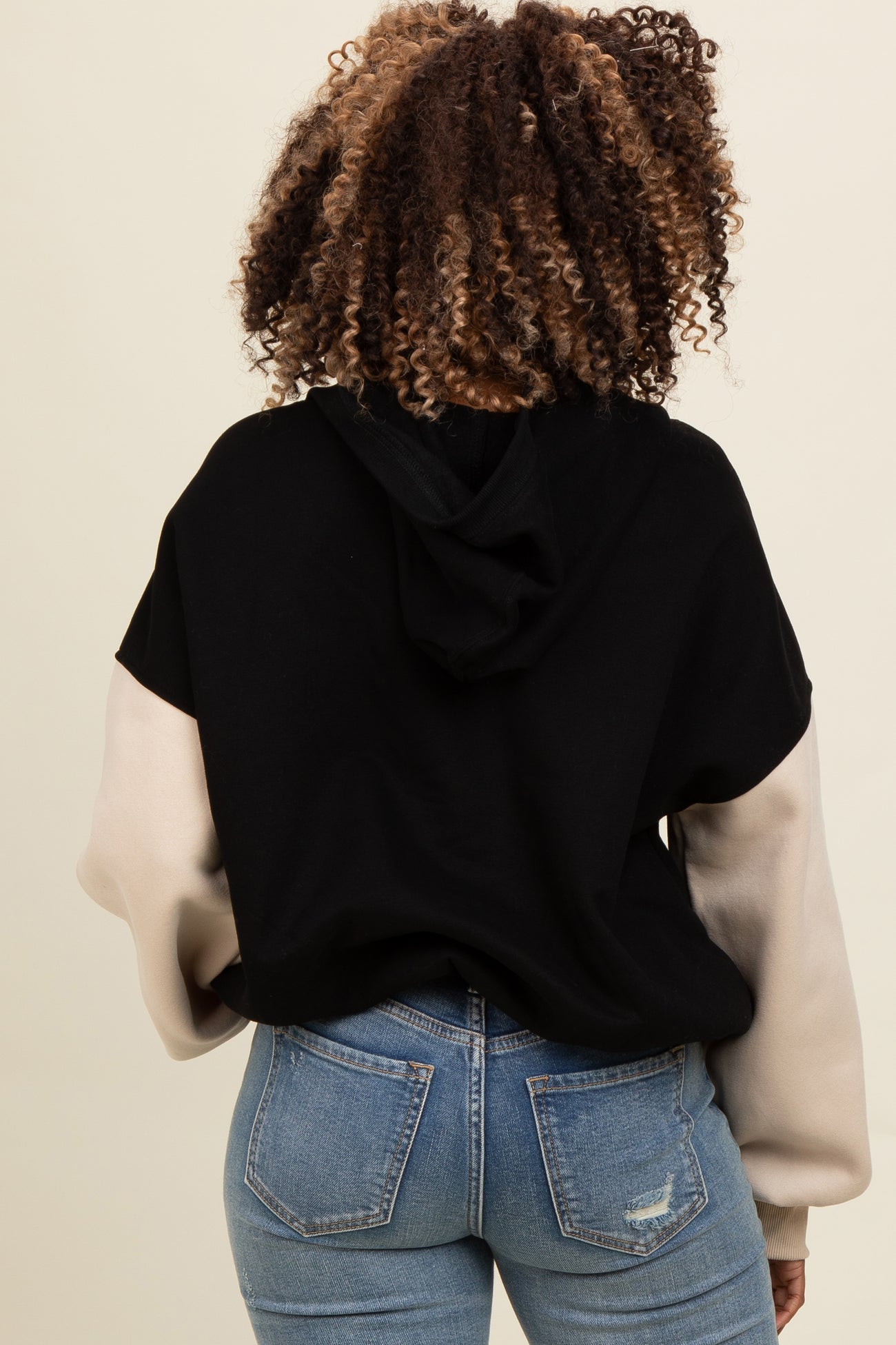 woman wearing a black and beige color block hoodie with a hood, paired with light wash denim jeans