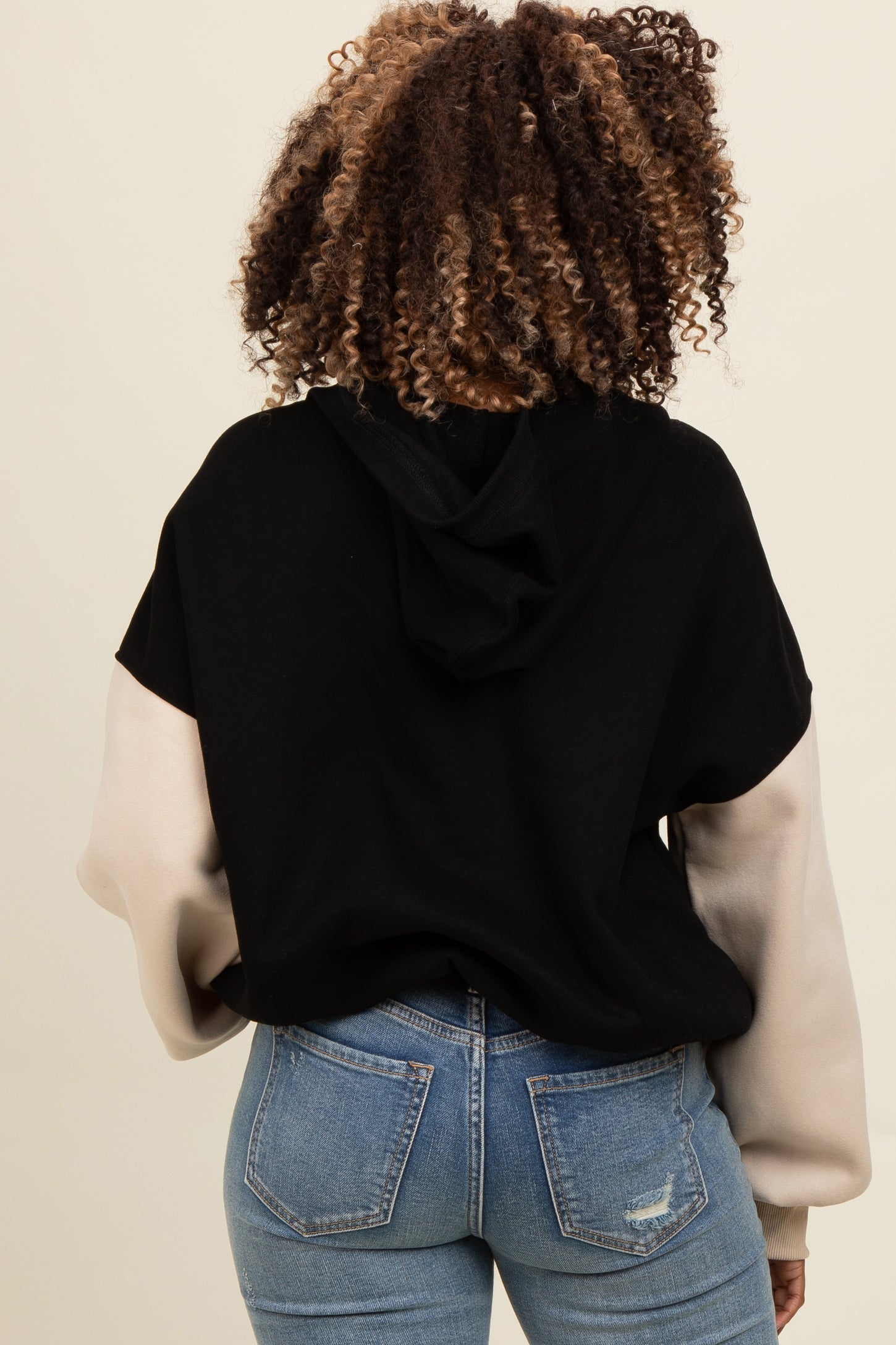 woman wearing a black and beige color block hoodie with a hood, paired with light wash denim jeans