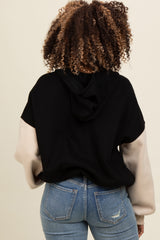 woman wearing a black and beige color block hoodie with a hood, paired with light wash denim jeans