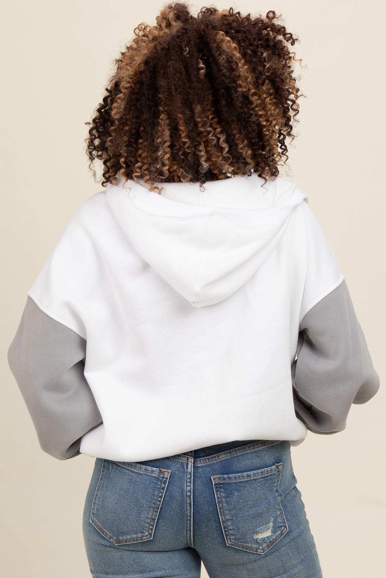 woman wearing a white and grey color block hoodie with a relaxed fit and a hood, viewed from the back