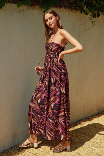 woman wearing a strapless maxi dress in a pink and purple abstract print, posing outdoors with a relaxed expression