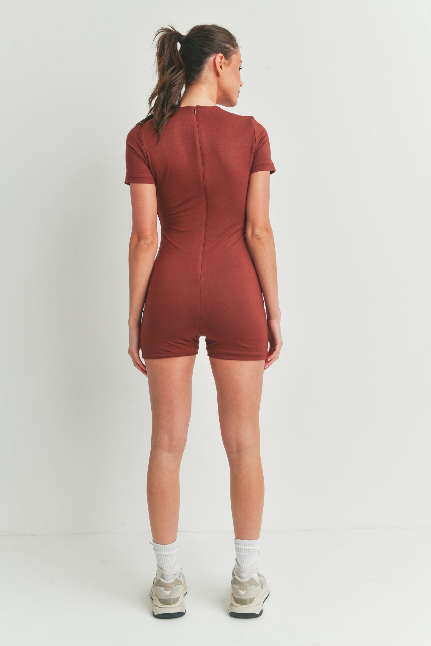 woman wearing a rust-colored short sleeve bodysuit, seen from the back with a fitted style and shorts length
