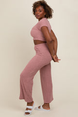 woman wearing a pink two-piece matching set with a cropped top and wide-leg pants, standing sideways with hands behind her back
