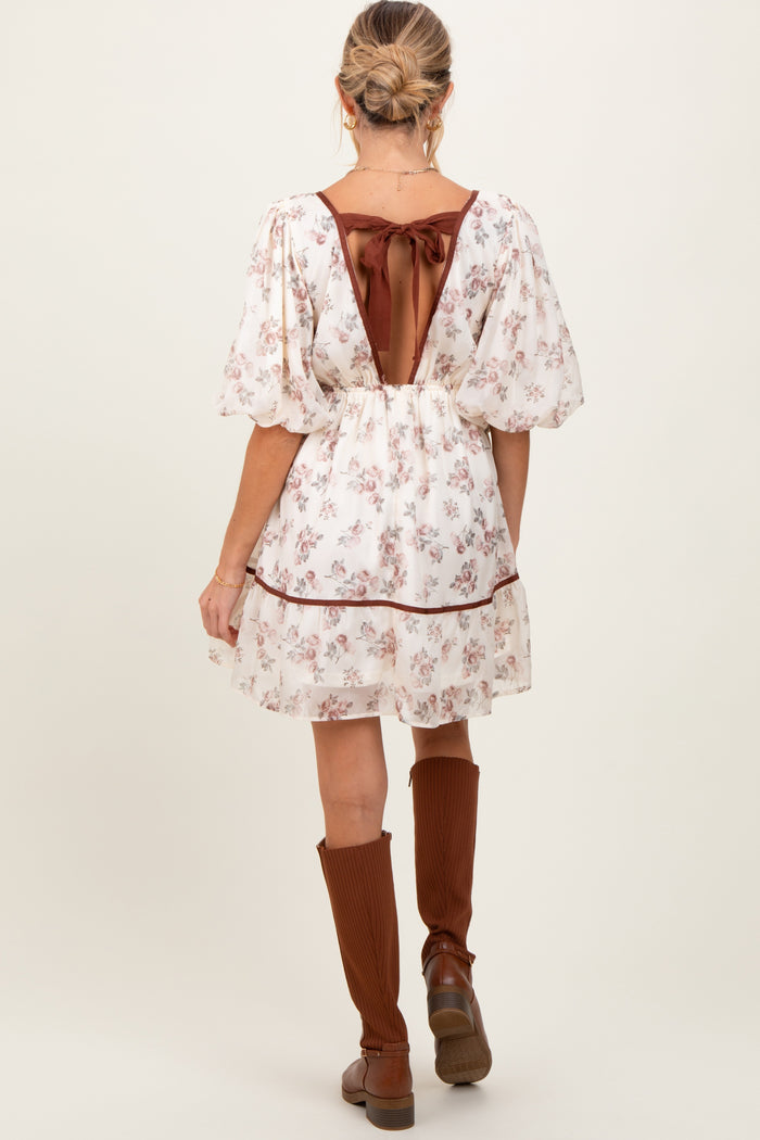 woman wearing a floral print short maternity dress with puff sleeves and a ribbon tie at the back