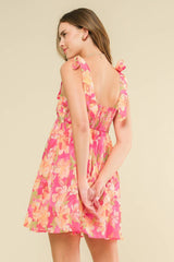 woman wearing a pink floral sundress with tie straps and a smocked back, standing with hands behind her back