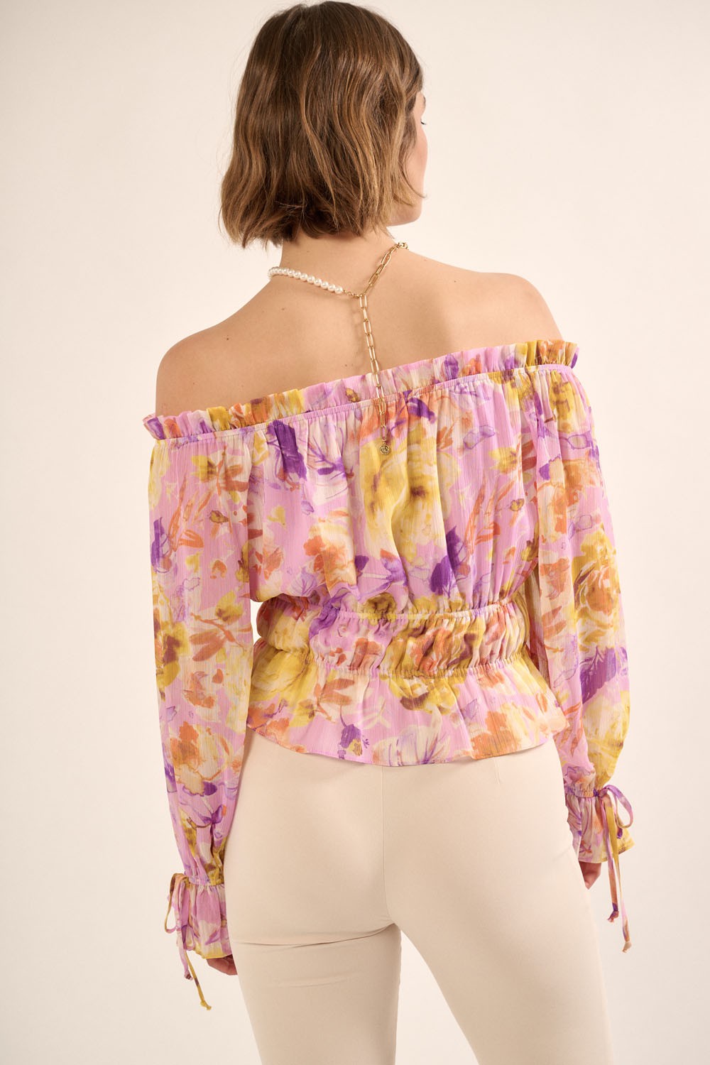 woman wearing a purple floral off-the-shoulder blouse with a cinched waist and long sleeves