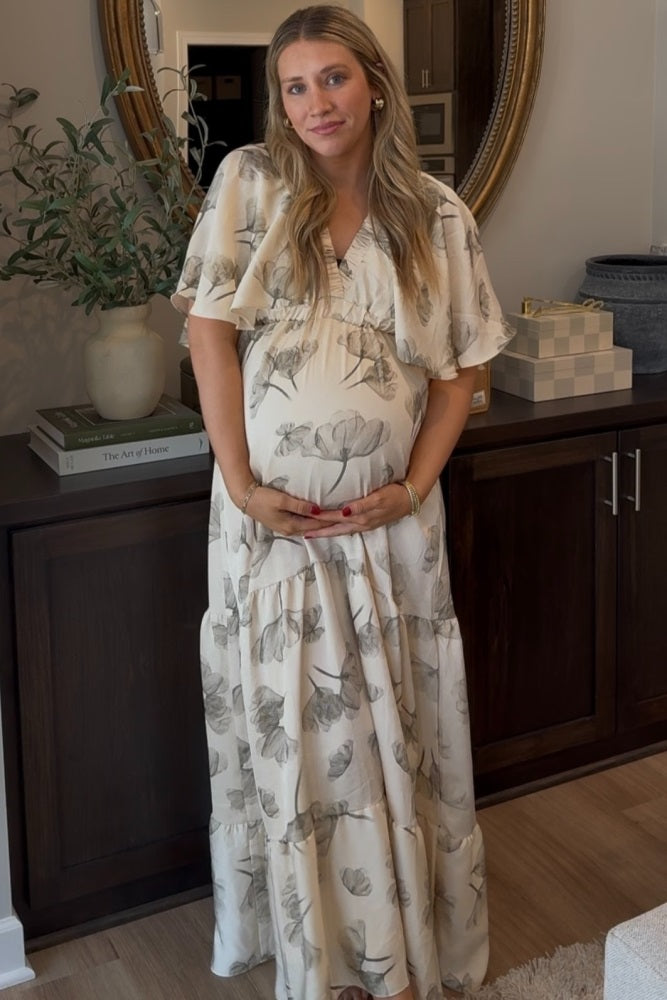 woman wearing a cream floral maternity maxi dress and holding her baby bump