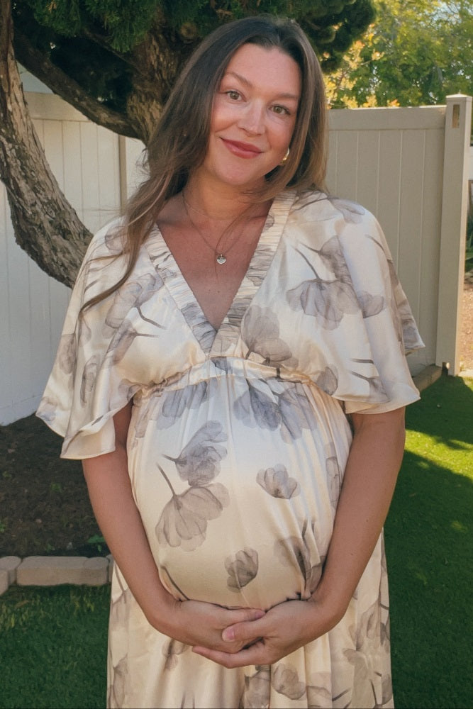 woman wearing a cream floral print maternity dress and holding her baby bump