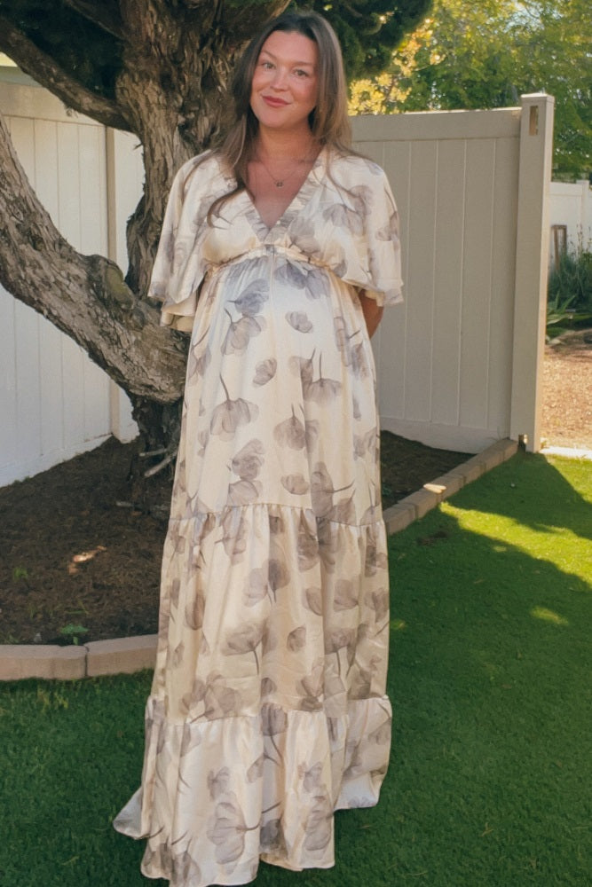 woman wearing a floral print maxi maternity dress with a v-neckline and short flutter sleeves, showing her baby bump
