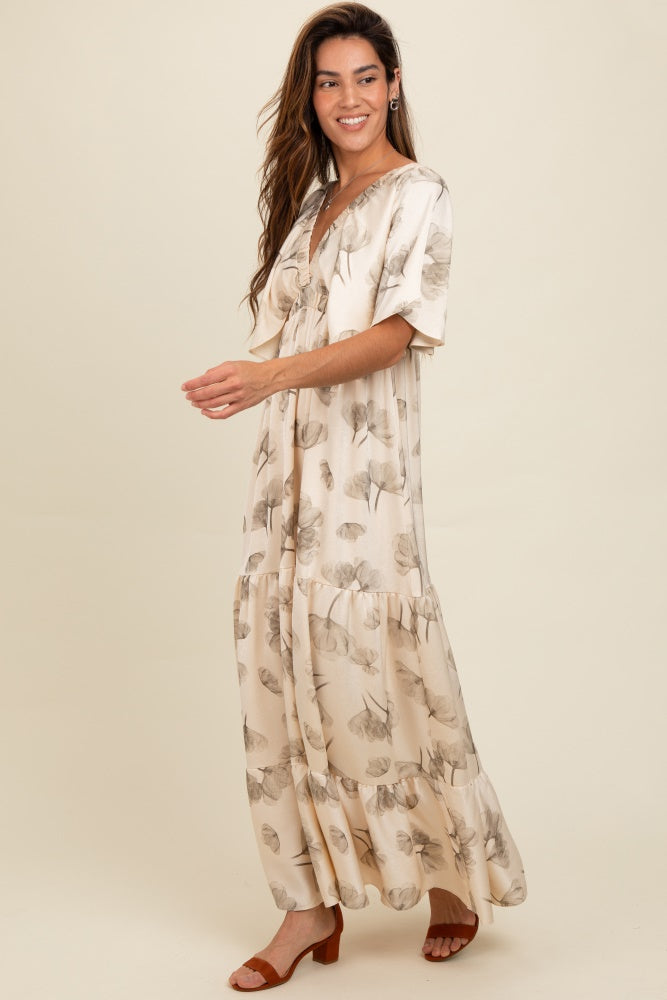 woman wearing a cream floral maxi dress with a v-neck and ruffle hem, standing in a light, airy pose