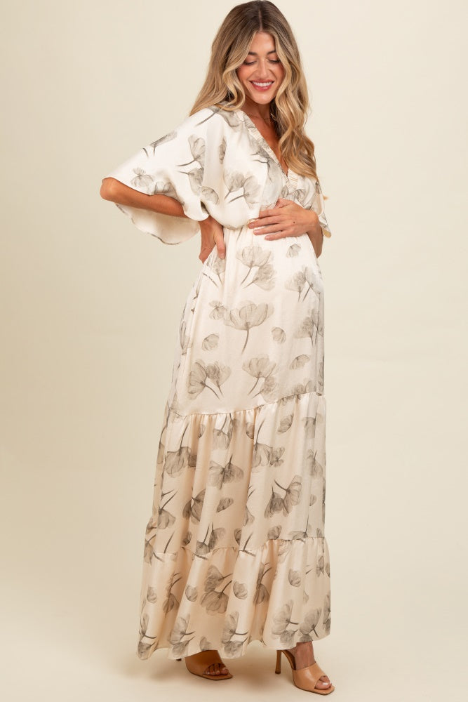 woman wearing a cream floral maternity maxi dress with flutter sleeves and a visible baby bump