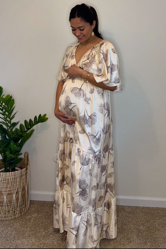 woman wearing a floral print maternity maxi dress and gently holding her baby bump