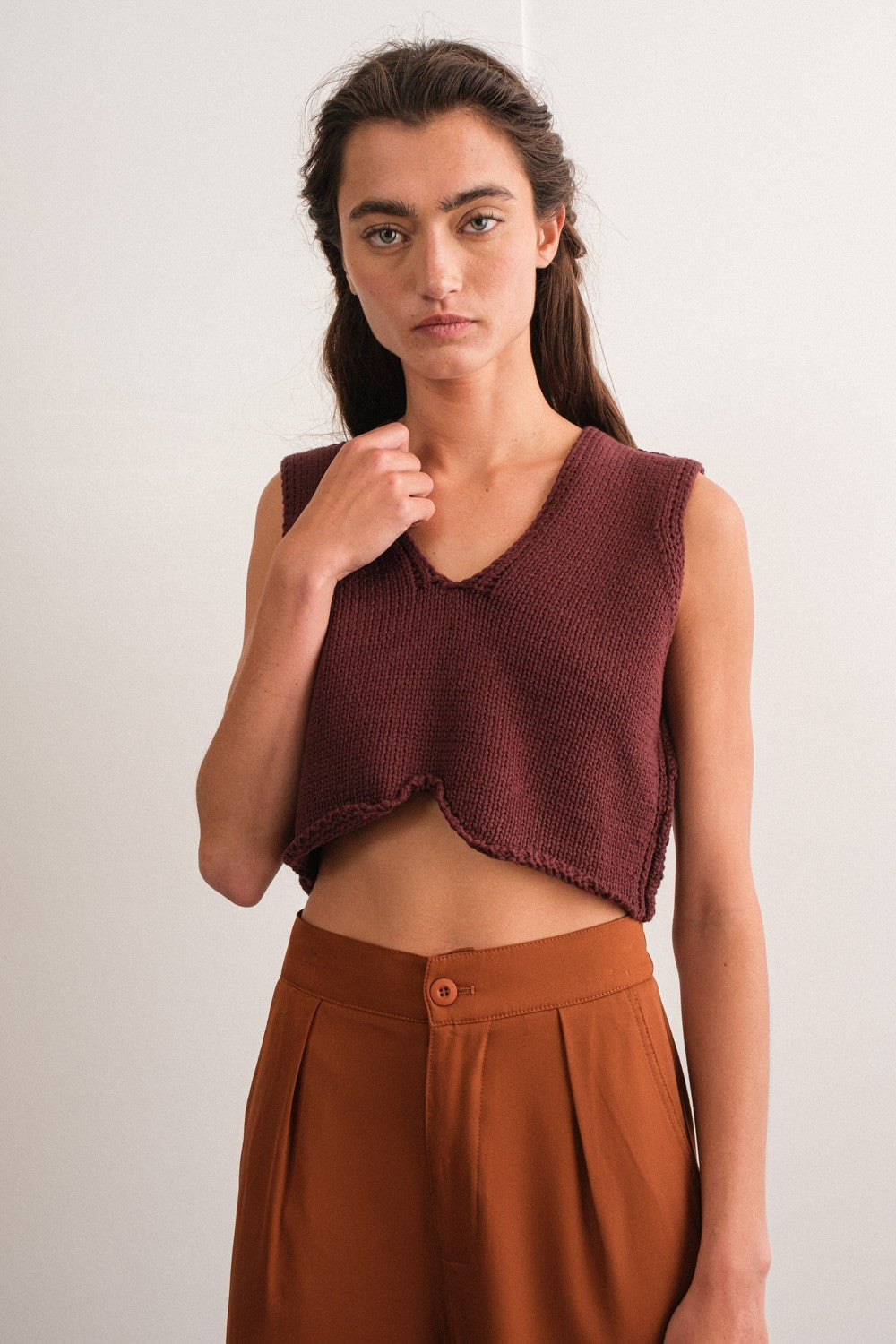 woman wearing a maroon cropped knitted top with a v-neck and high-waisted brown pants.