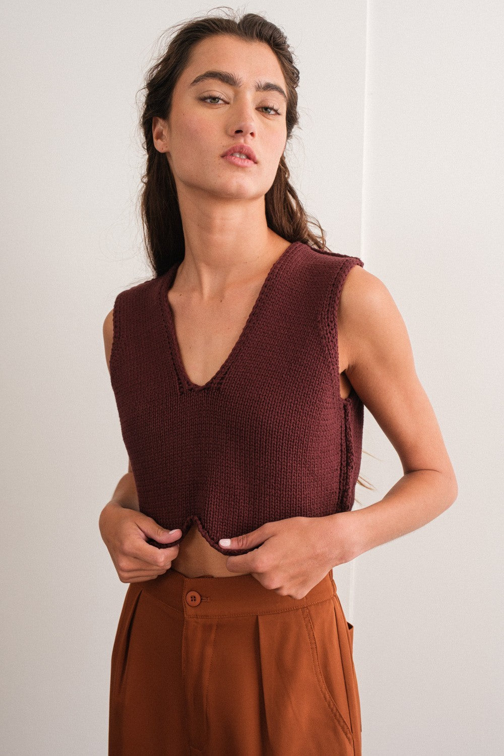 woman wearing a burgundy sleeveless v-neck knit top paired with high-waisted brown trousers