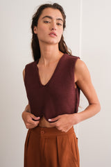 woman wearing a burgundy sleeveless v-neck knit top paired with high-waisted brown trousers