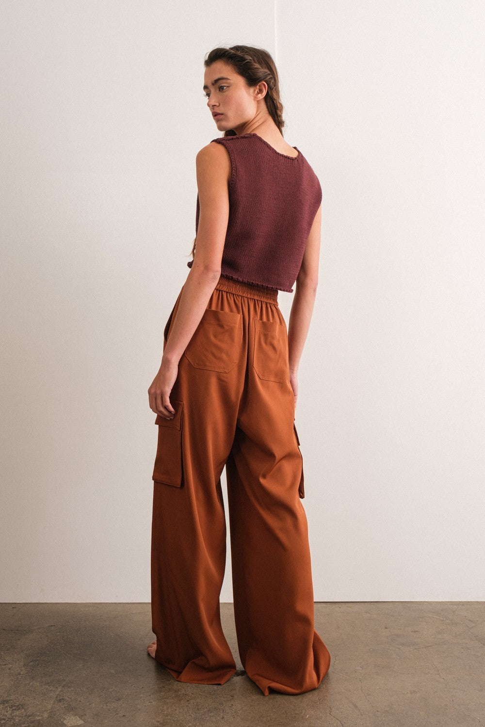 woman wearing a maroon sleeveless cropped sweater and rust-colored wide-leg cargo pants, seen from the back