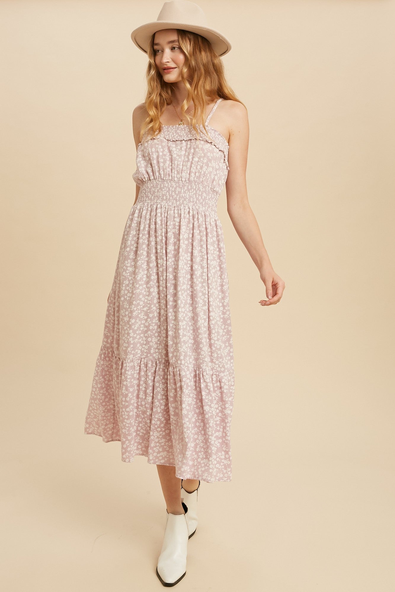 woman wearing a pink floral maxi dress with smocked bodice and tiered skirt, styled with a hat and white ankle boots