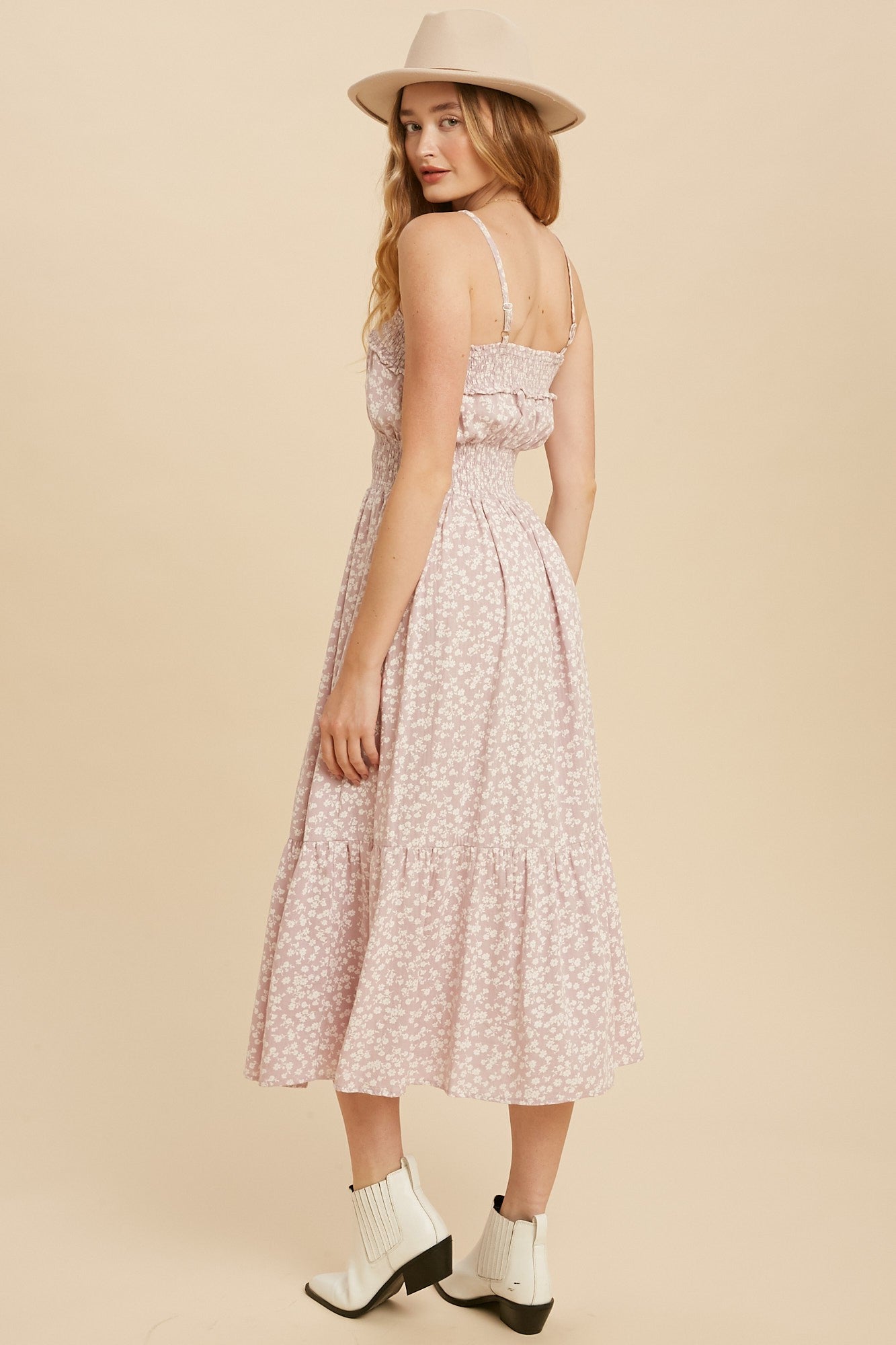 woman wearing a pink floral midi dress with spaghetti straps and a ruffled hem, styled with a wide-brimmed hat and ankle boots