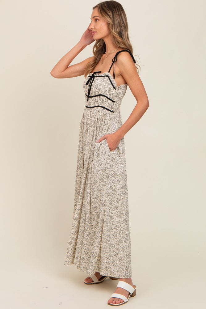 woman wearing a cream floral maxi dress with black straps and pockets, standing against a plain background