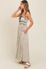 woman wearing a cream floral maxi dress with black straps and pockets, standing against a plain background