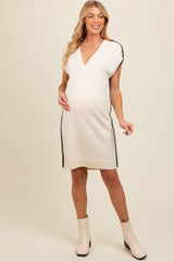woman wearing a cream maternity dress with black side detailing and a v-neck, showcasing her baby bump