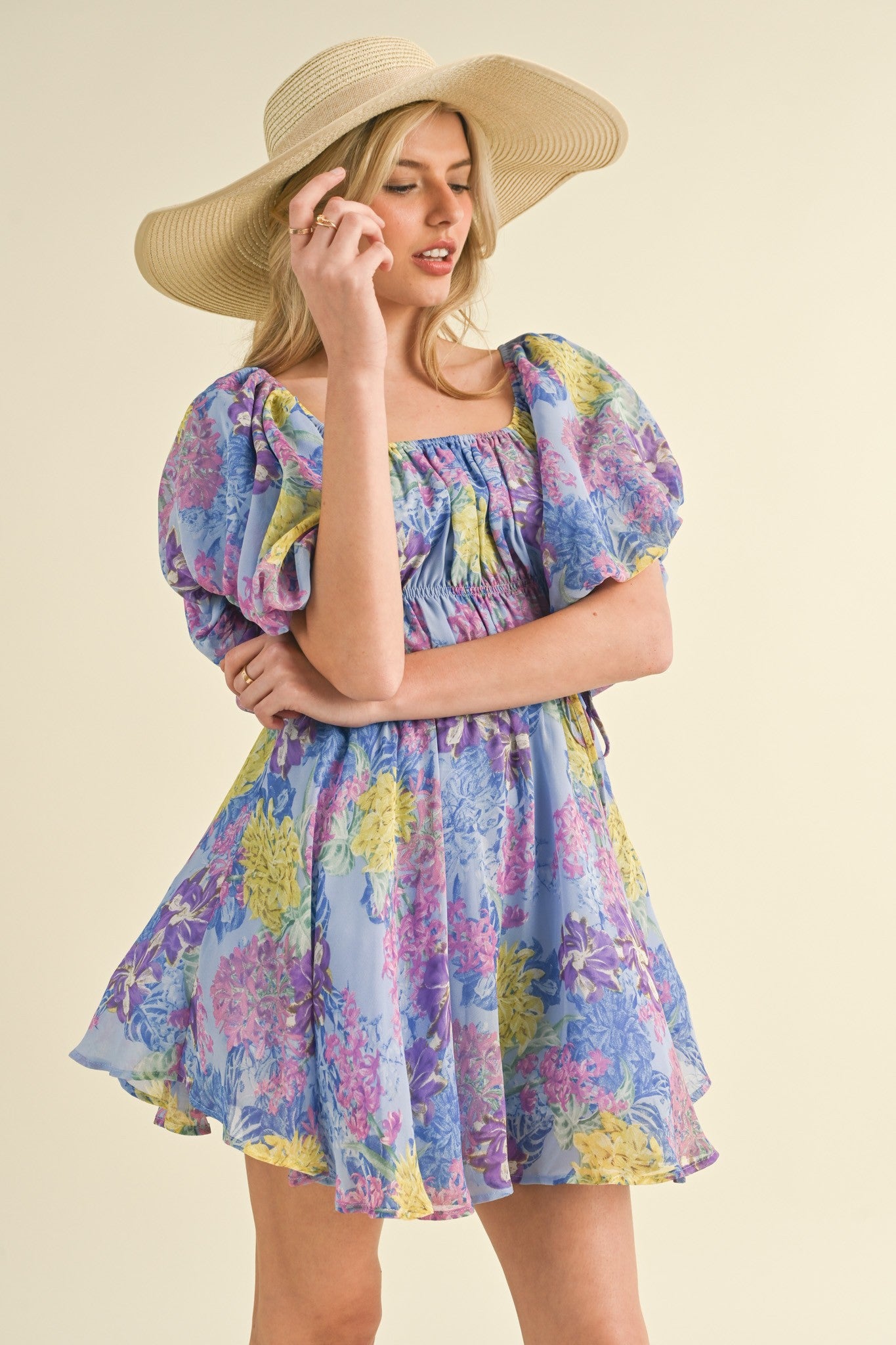 woman wearing a purple floral puff sleeve mini dress and a wide-brimmed straw hat
