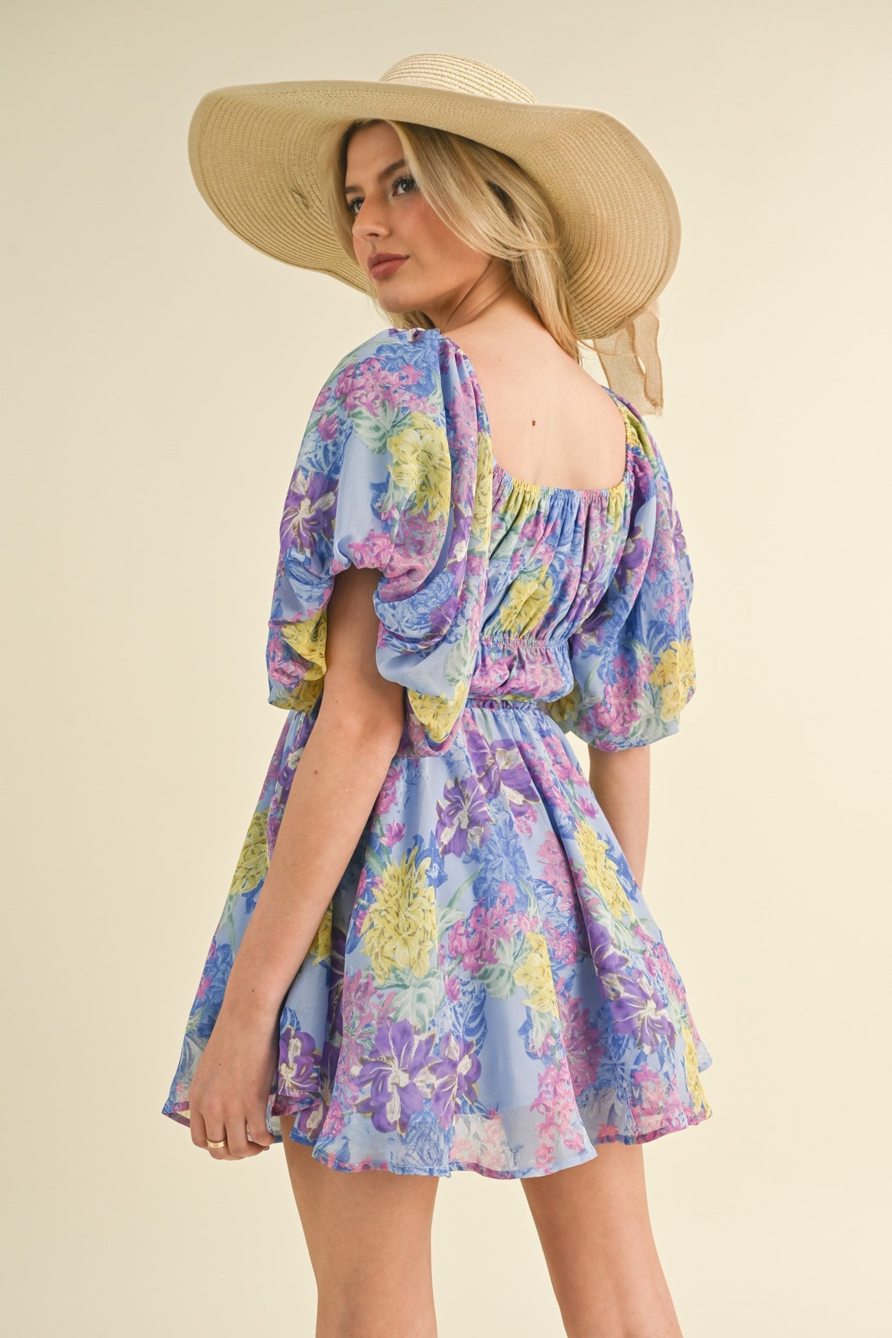 woman wearing a floral mini dress in pastel colors with puff sleeves and a square neckline, styled with a wide-brimmed hat