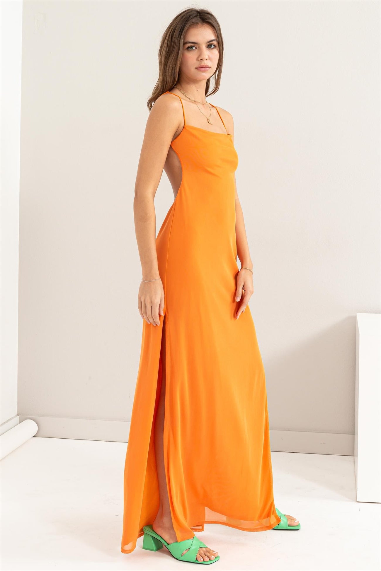 woman wearing an orange slip dress with side slits and green strappy heels