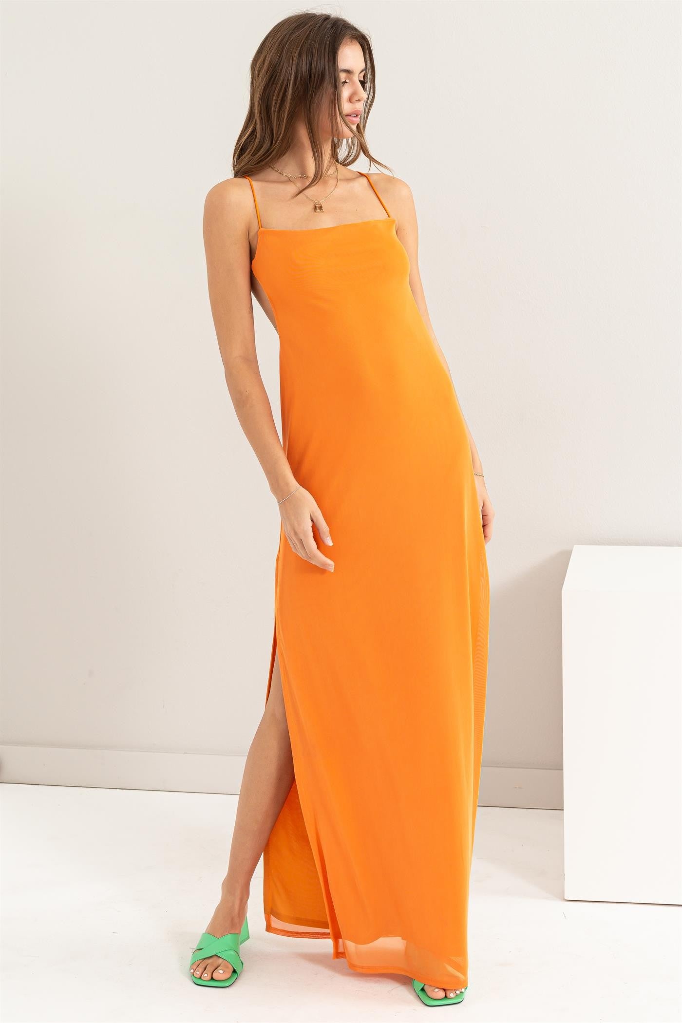 woman wearing an orange sleeveless maxi dress with a side slit and minimalist straps