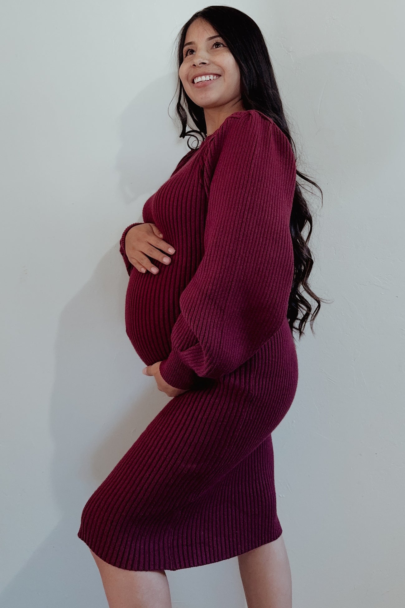 woman wearing a burgundy ribbed maternity dress and holding her baby bump