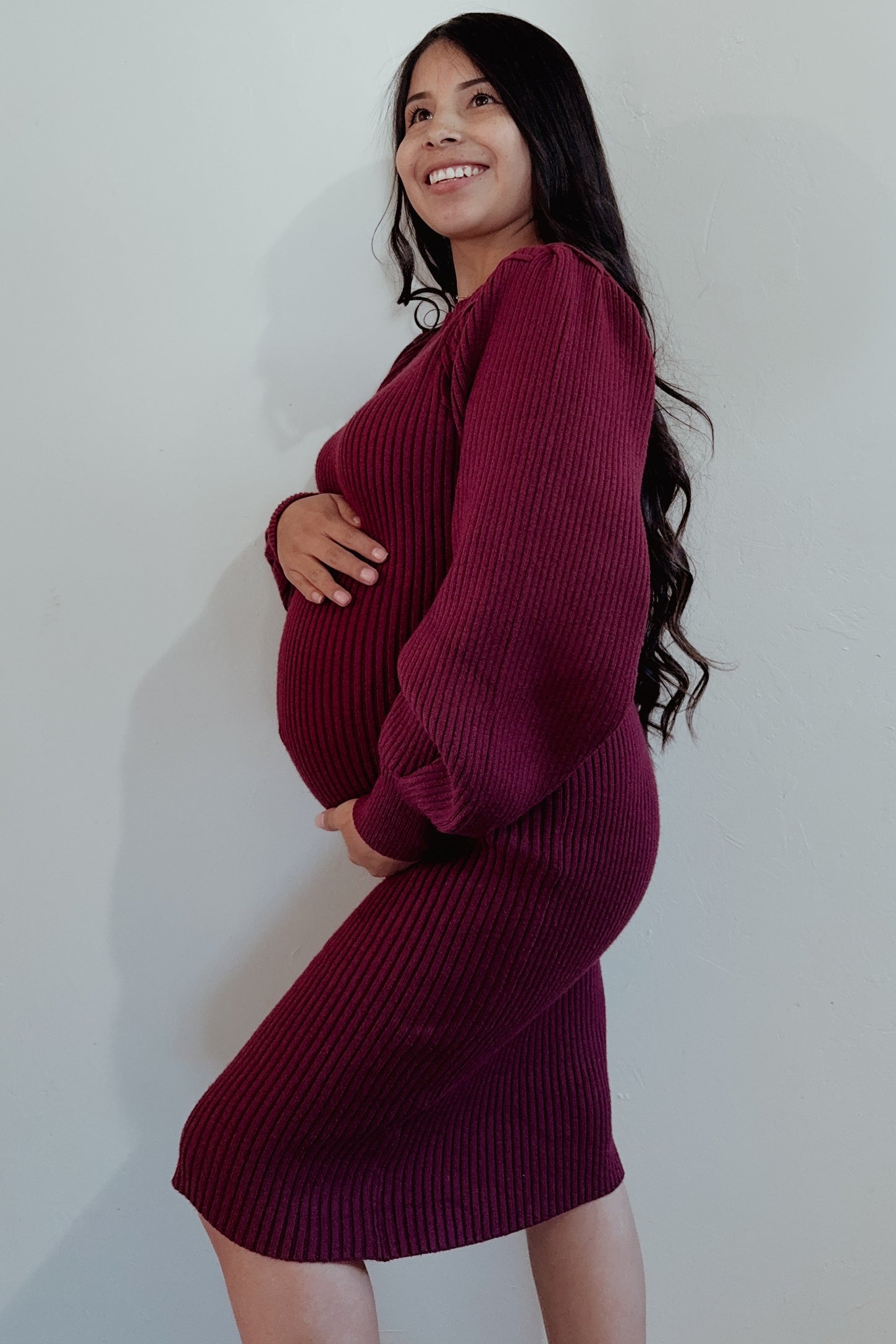 woman wearing a burgundy ribbed maternity dress and holding her baby bump