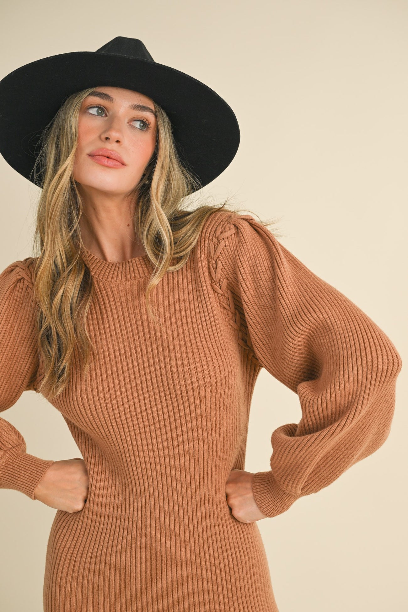 woman wearing a rust ribbed knit sweater dress with puff sleeves and a black wide-brim hat
