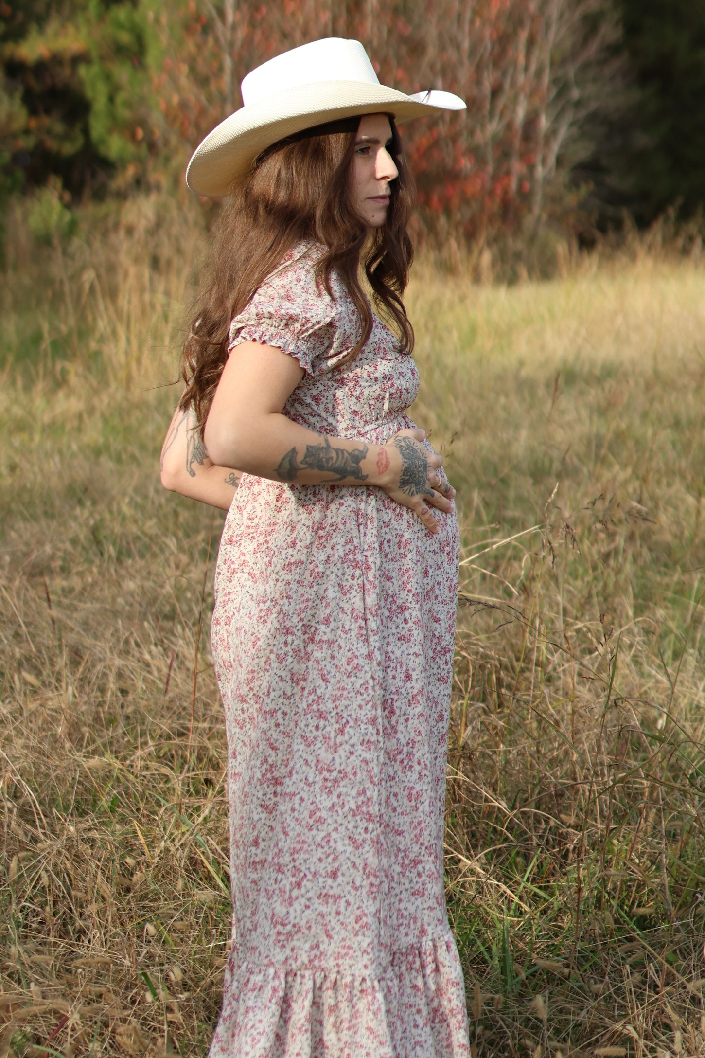 woman wearing a floral pink maternity maxi dress and holding her baby bump while standing in a field