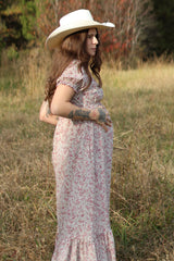 woman wearing a floral pink maternity maxi dress and holding her baby bump while standing in a field