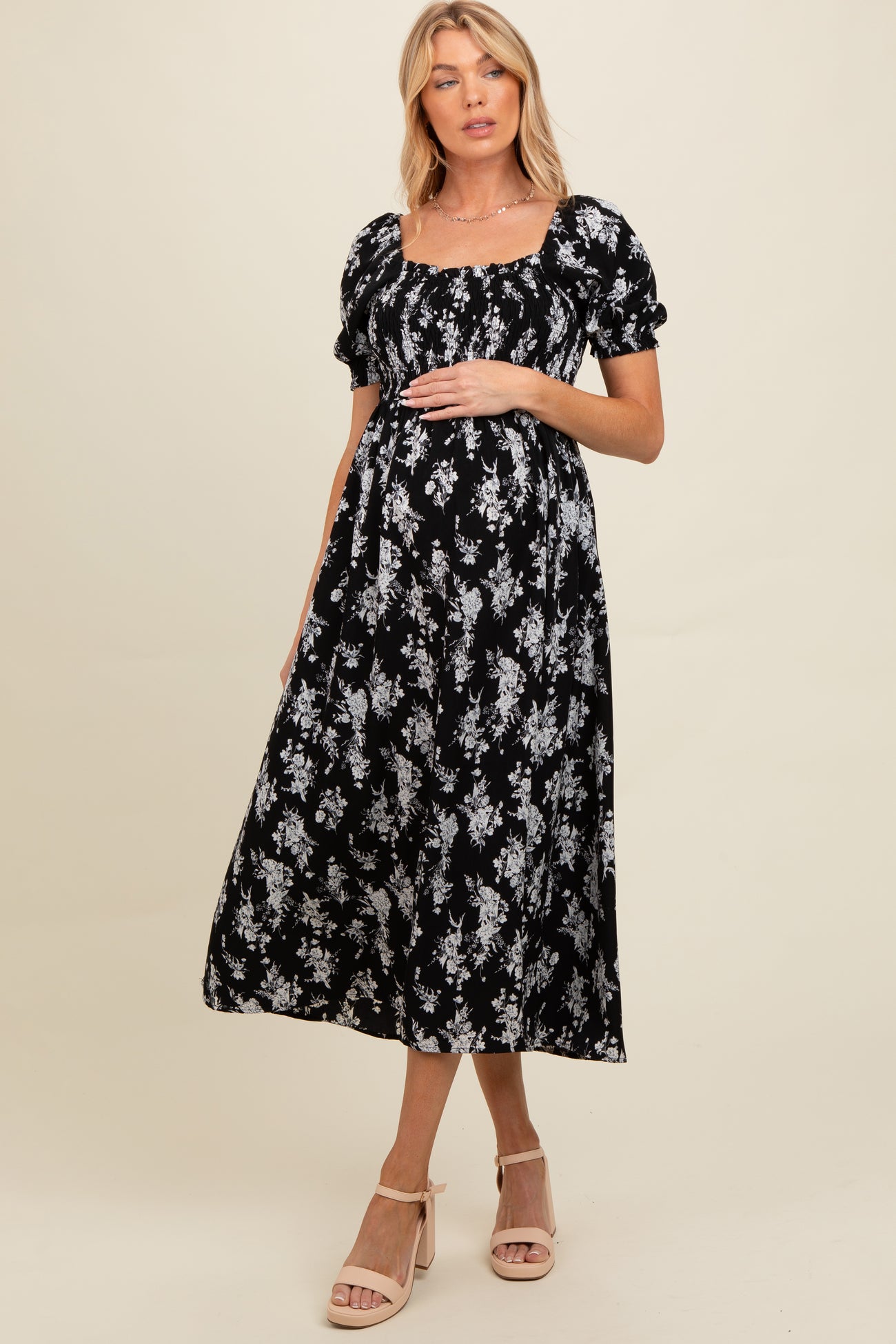 woman wearing a black floral maternity dress with puff sleeves and a square neckline, holding her baby bump