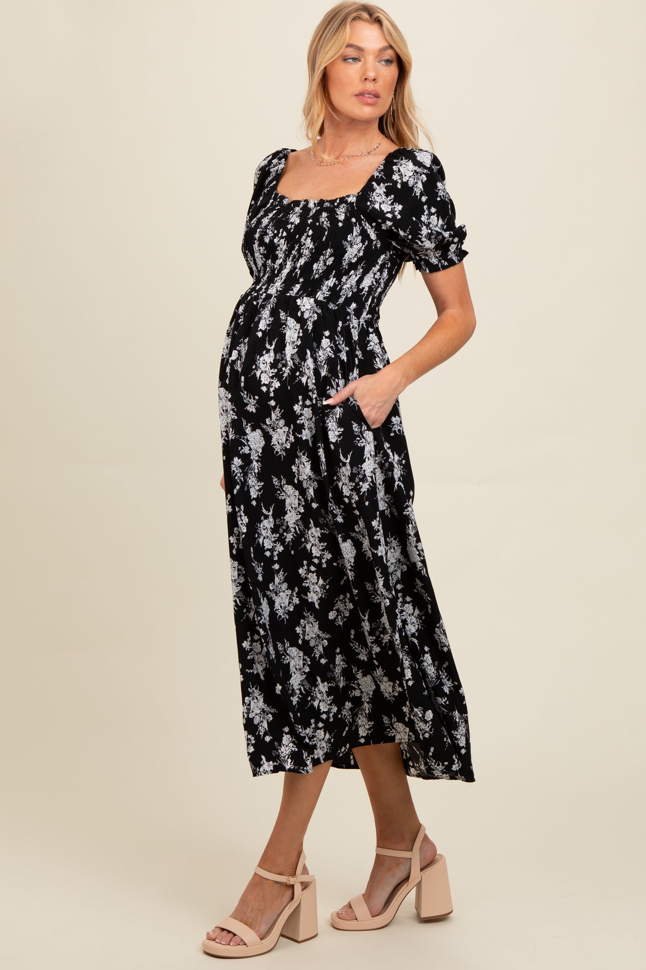 woman wearing a black floral print maternity dress with puff sleeves and pockets, showing her baby bump
