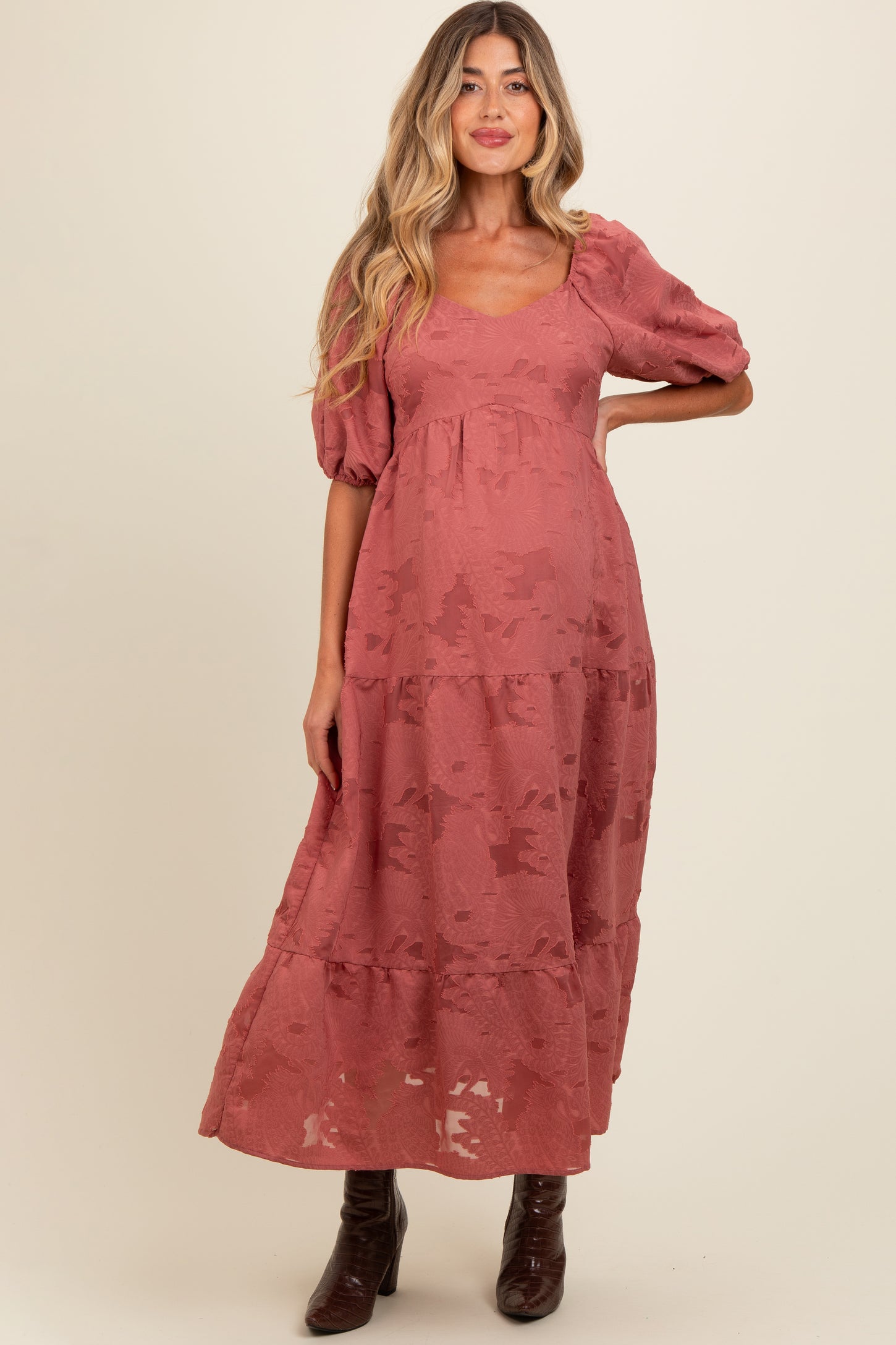 woman wearing a rust-colored maternity maxi dress with puff sleeves and tiered design, showing her baby bump