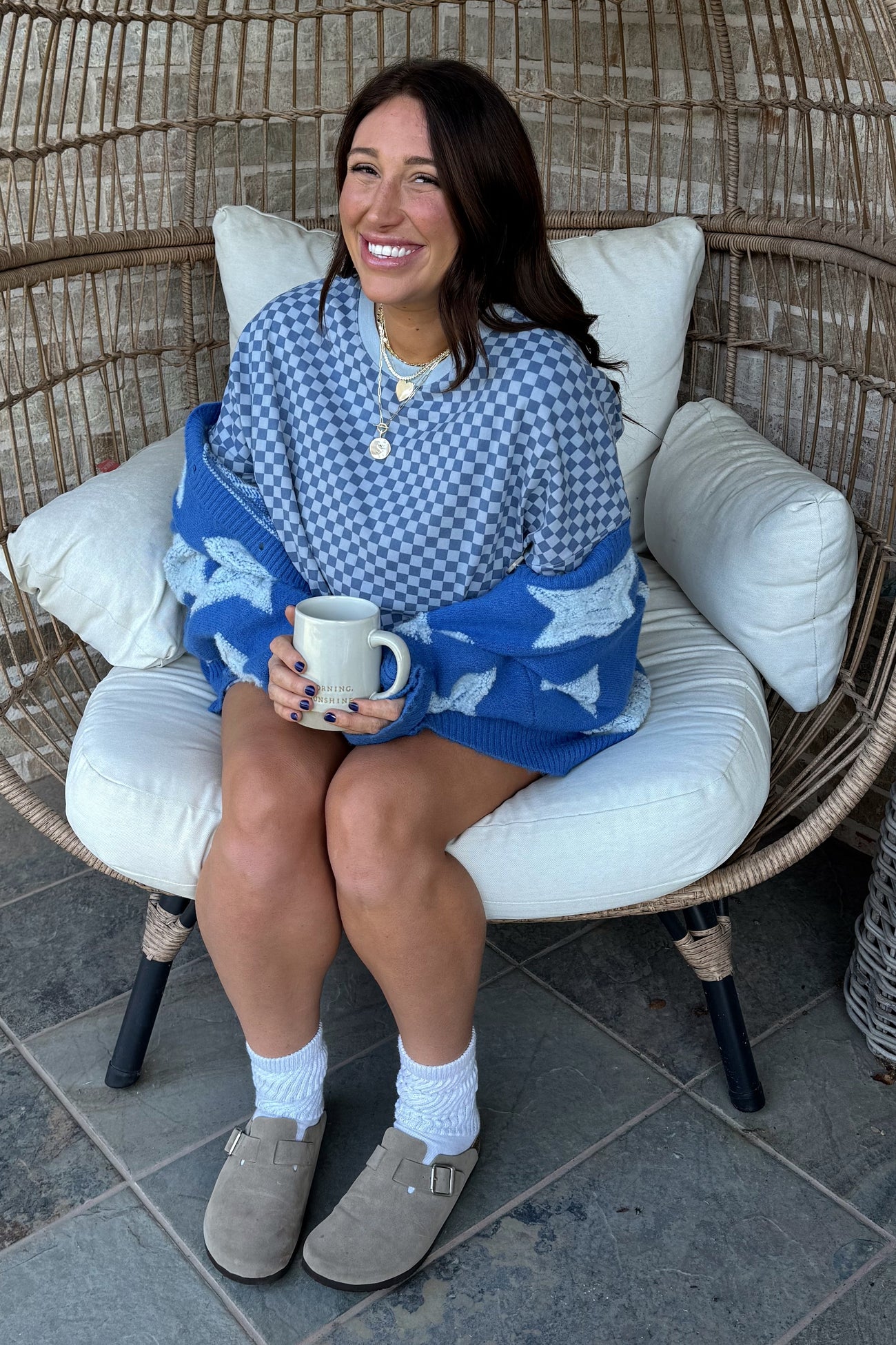 woman sitting in a chair wearing a checkered oversized sweater and a blue star-patterned blanket, holding a mug