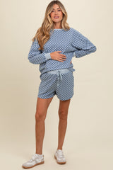 woman wearing a blue checkered maternity sweatshirt and shorts, holding her baby bump