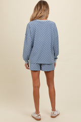 woman wearing a blue checkered maternity loungewear set consisting of a long sleeve top and matching shorts, back view