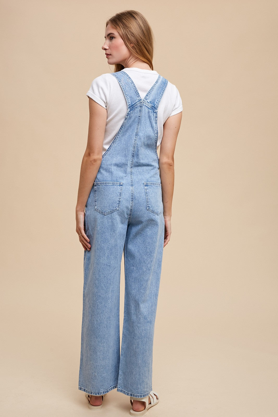 woman wearing light blue denim overalls with wide legs and a white t-shirt, viewed from the back