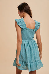 woman wearing a teal shirred back mini dress with ruffle sleeves and a tiered skirt