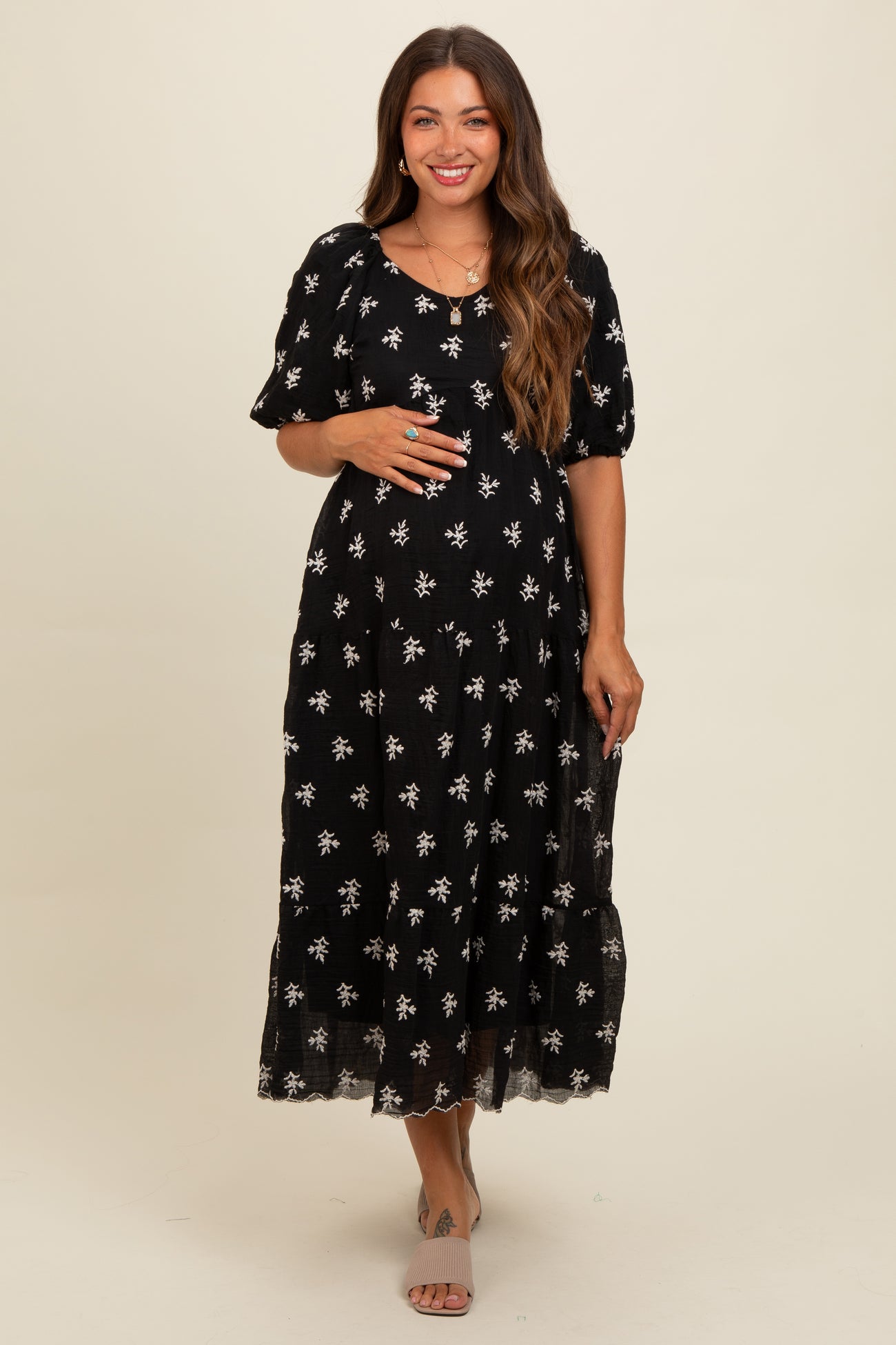 woman wearing a black maternity dress with white floral patterns and puff sleeves, showcasing her baby bump